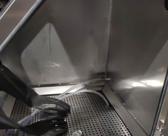 Technician using vapour blasting equipment to clean and finish metal components inside cabinet